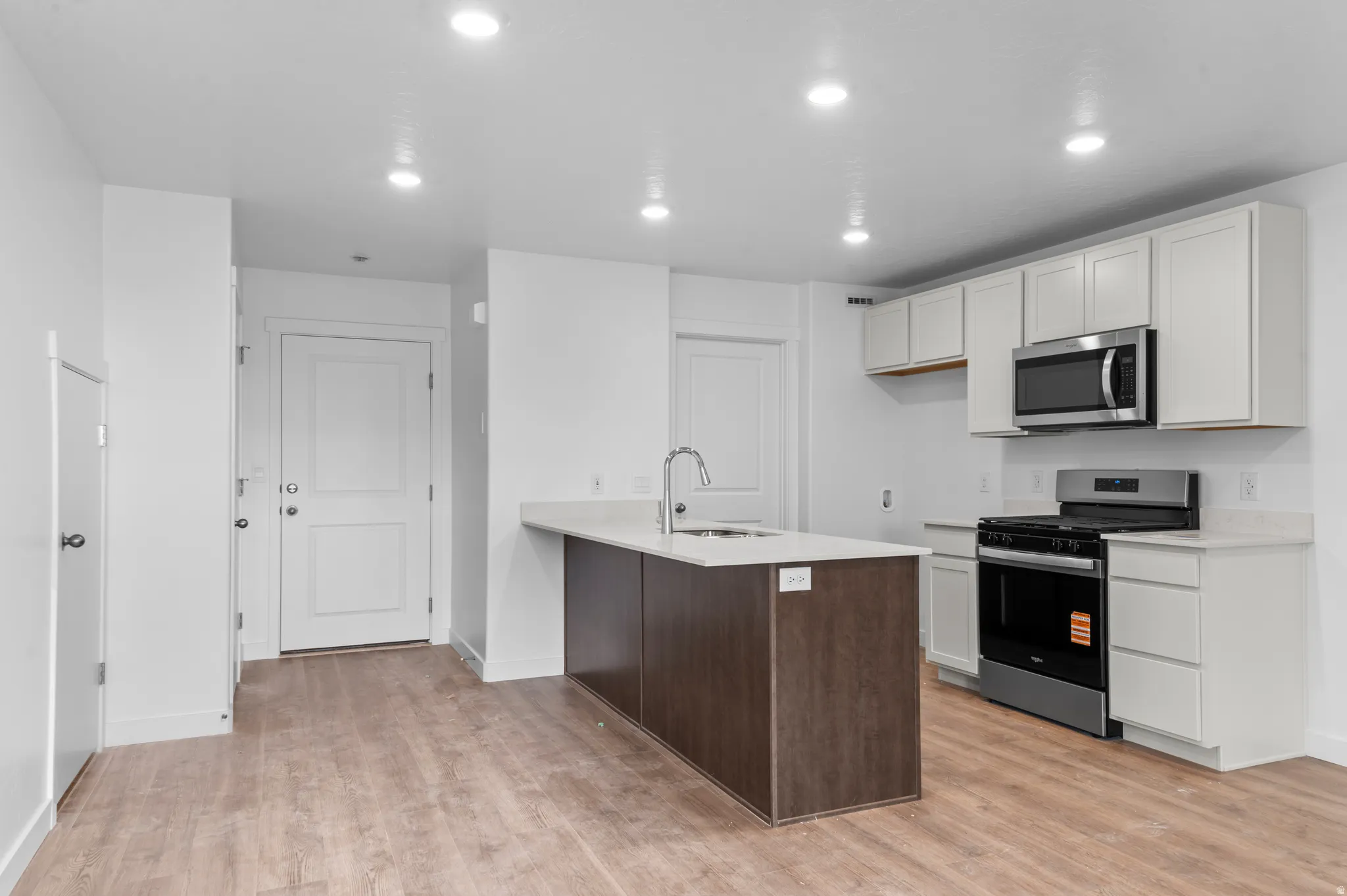 Kitchen featuring light wood-finish flooring, white cabinetry, stainless steel appliances, and a central island with a sink and a light-toned countertop