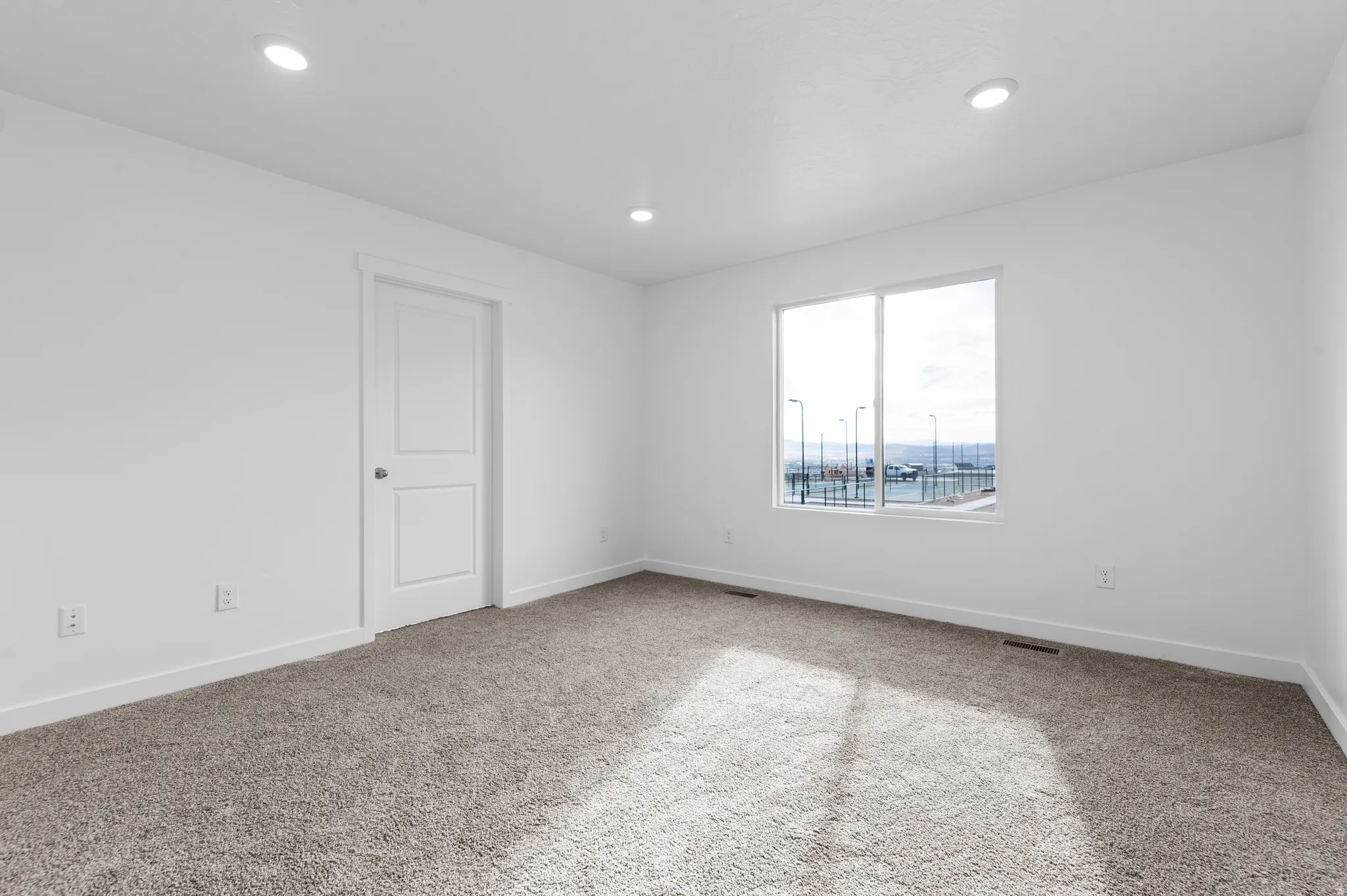 Recessed lighting, white interior walls, white trim, white two-panel door, and gray carpeting