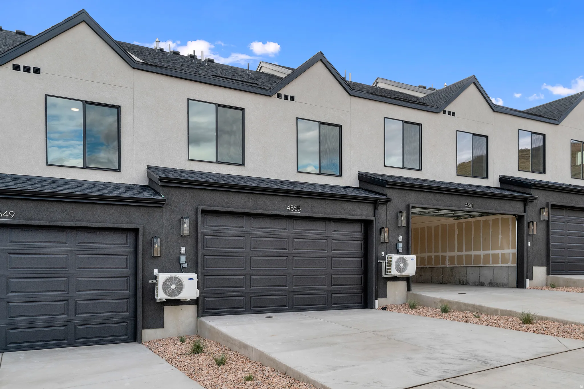 Contemporary exterior with light stucco and dark trim, featuring individual garage doors and concrete driveways