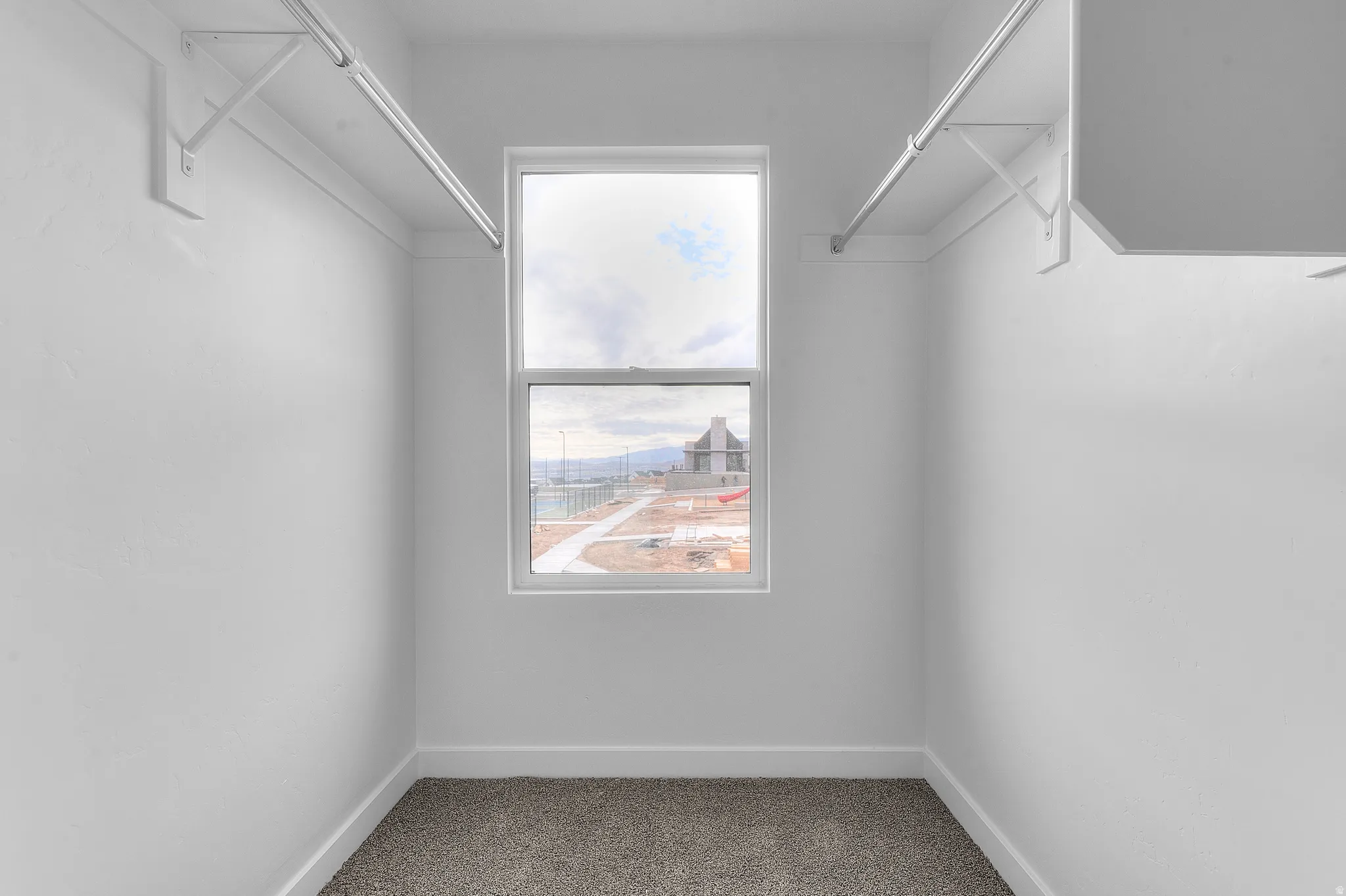 Carpeted flooring, white walls, built-in shelving, hanging rods, and a white-framed window