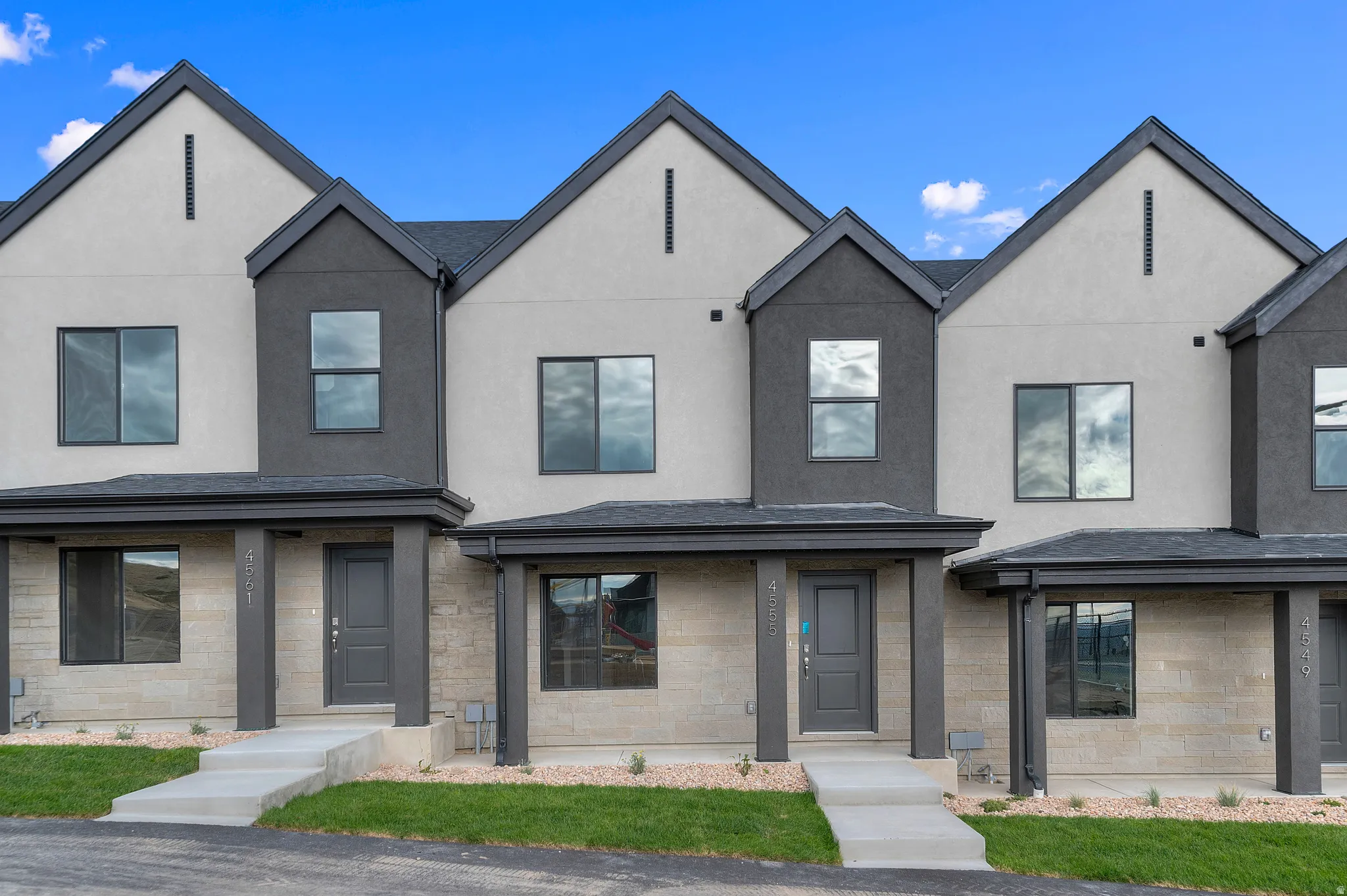 Modern townhouse exterior featuring a neutral stucco and stone facade, dark trim, gabled rooflines, and a covered entry