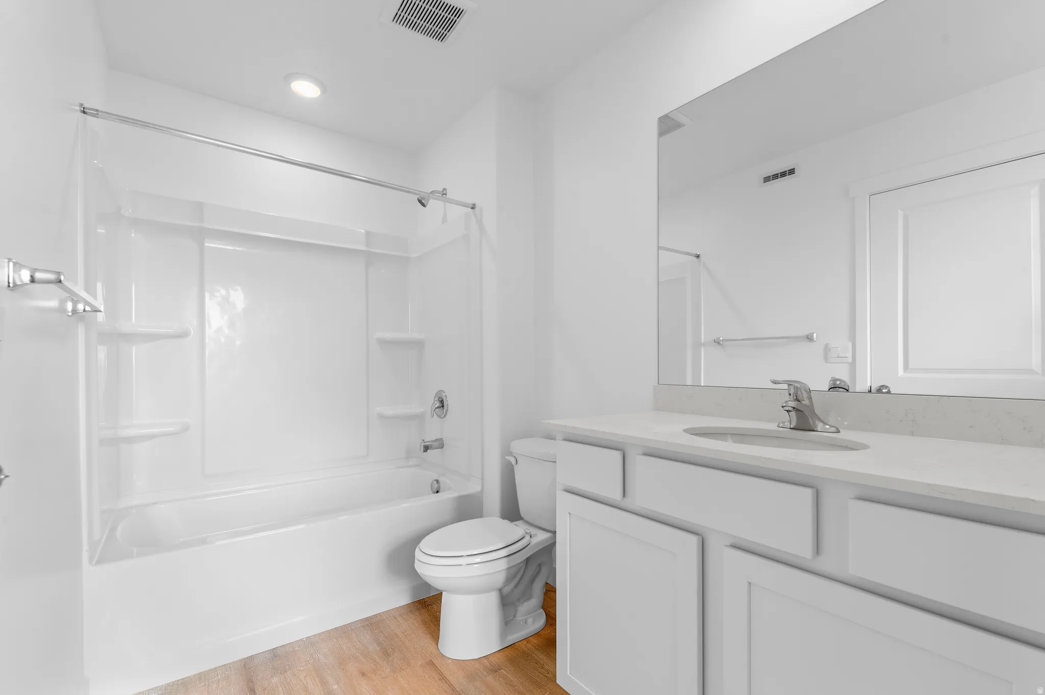 Bathroom featuring a full-size tub with shower, single vanity with light-toned countertop, integrated sink, large wall-mounted mirror, and wood-finish flooring