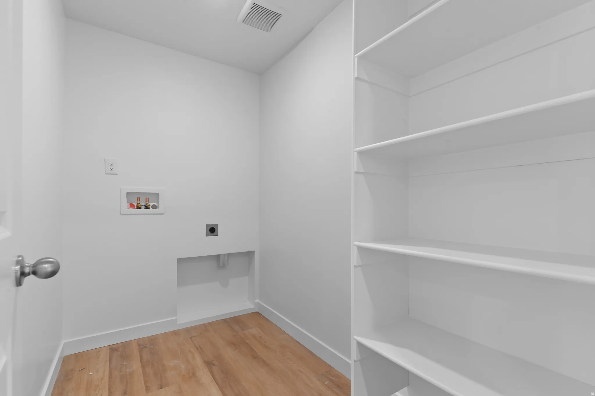 Dedicated utility space featuring wood-finish flooring, built-in shelving, and white walls