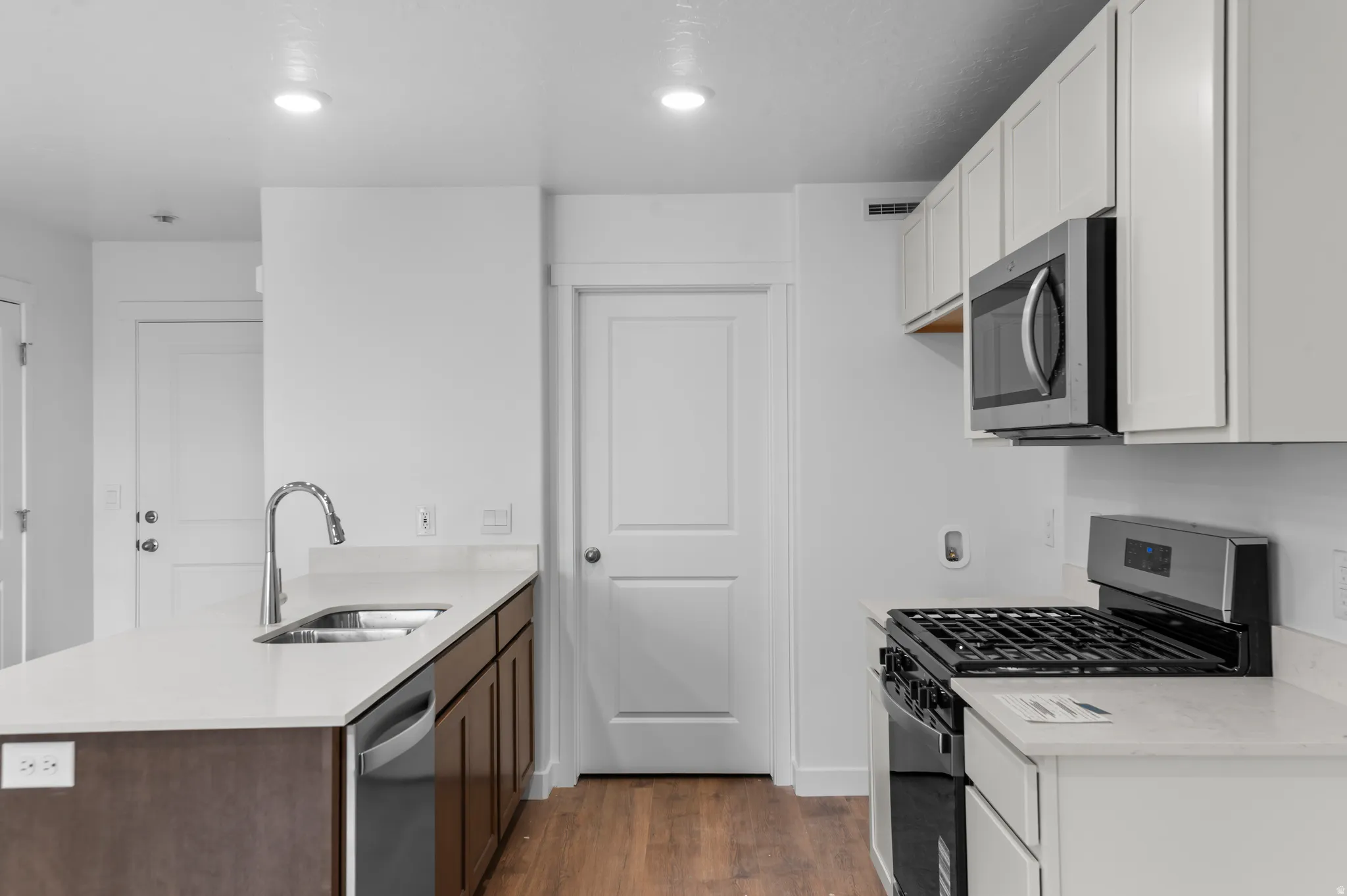 Kitchen featuring white cabinetry, light countertops, wood-finish flooring, stainless steel appliances, and a kitchen island with an integrated sink