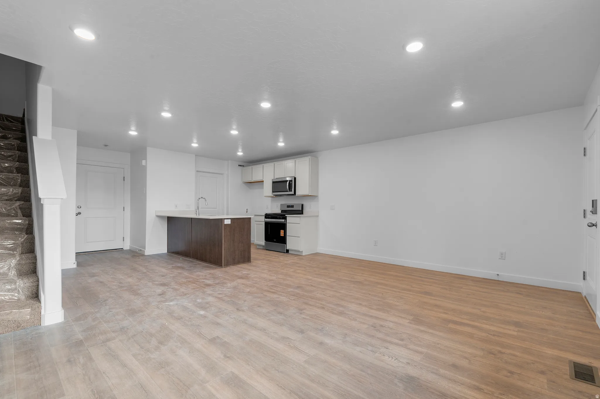 Open-concept living area featuring wood-finish flooring, recessed lighting, and a modern kitchen island with an integrated sink
