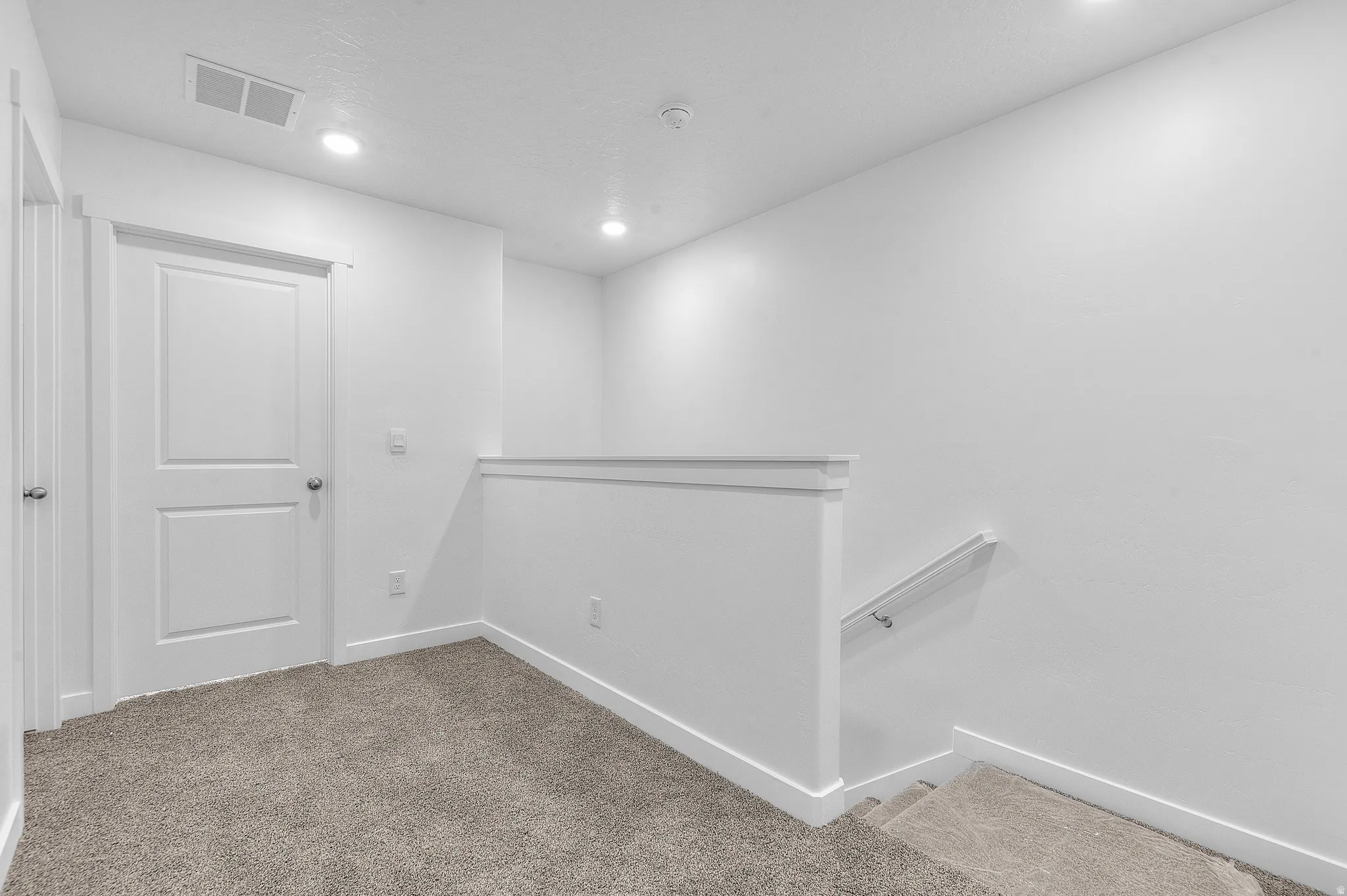 Neutral white walls with recessed ceiling lighting, textured carpeting, contemporary interior door, and a staircase with a handrail