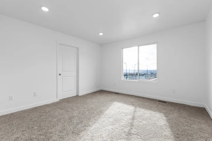 Recessed lighting, white interior walls, white trim, white two-panel door, and gray carpeting