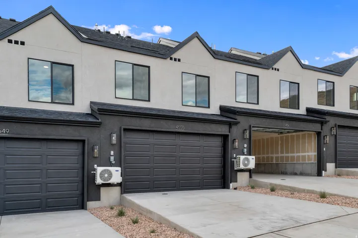 Contemporary exterior with light stucco and dark trim, featuring individual garage doors and concrete driveways