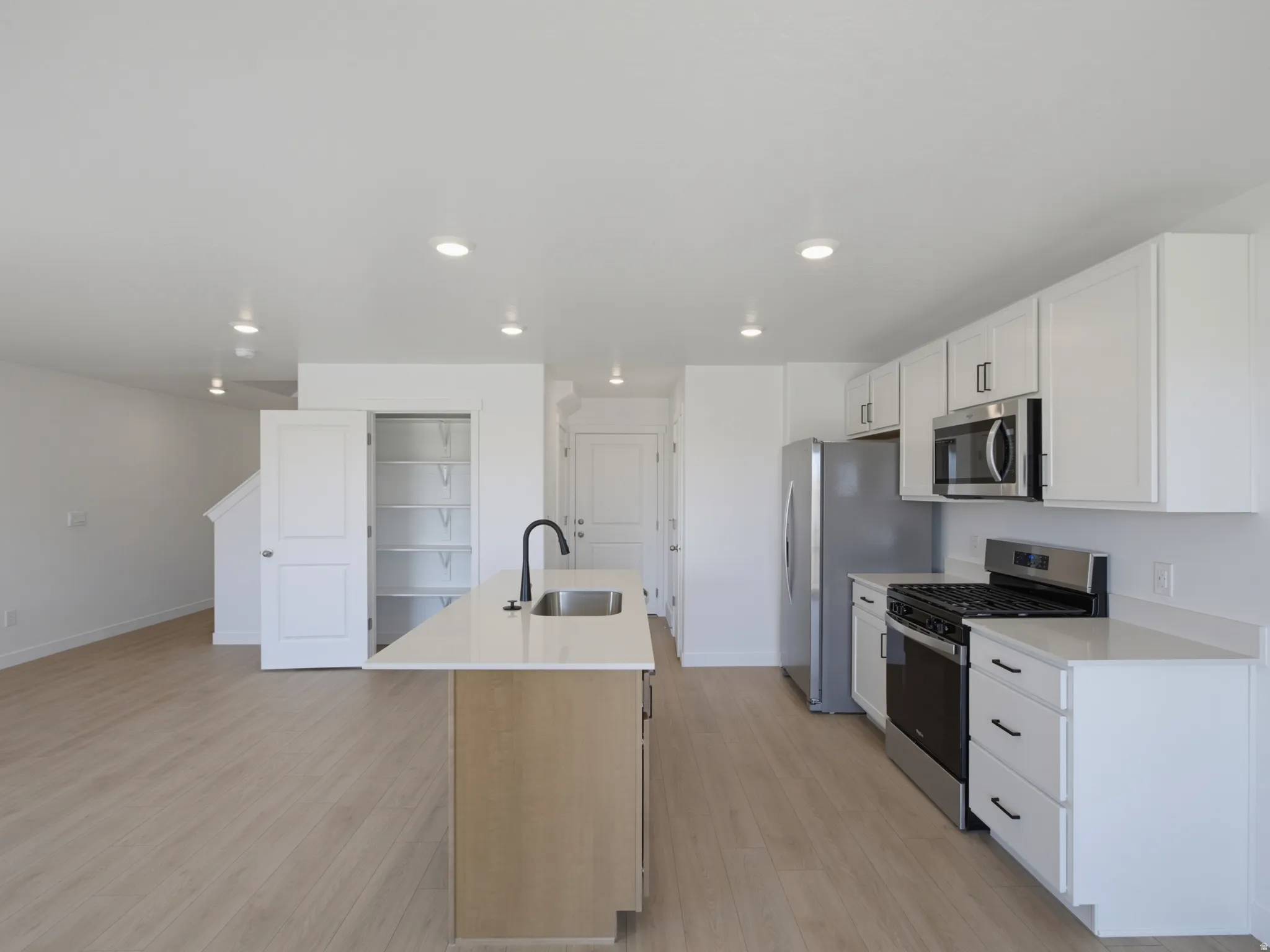 Kitchen with stainless steel appliances, white cabinetry, wood-finish flooring, and a central island with a sink