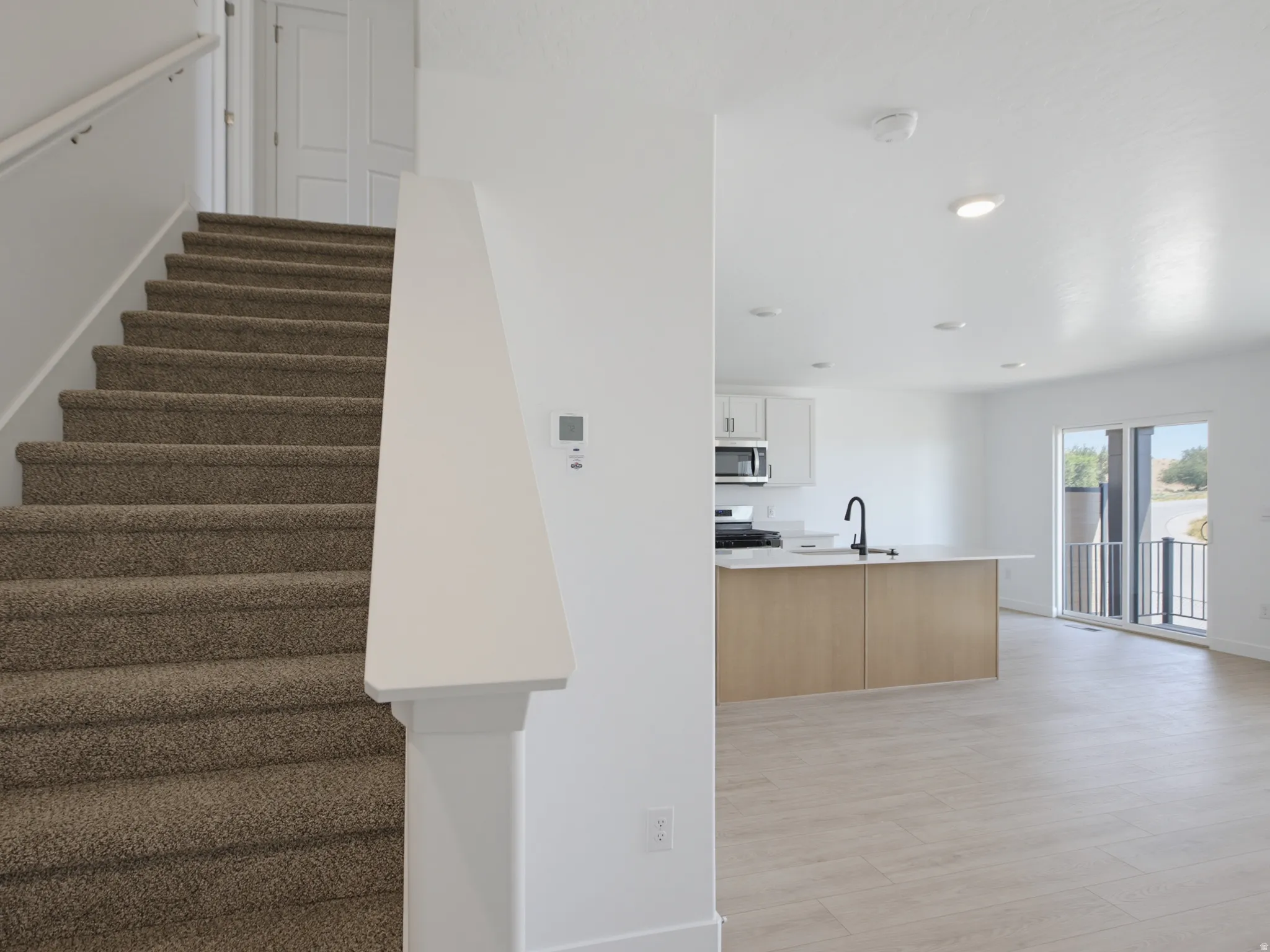 Carpeted staircase with white handrail, recessed lighting, wood-finish flooring, white cabinetry, and a kitchen island with a black faucet