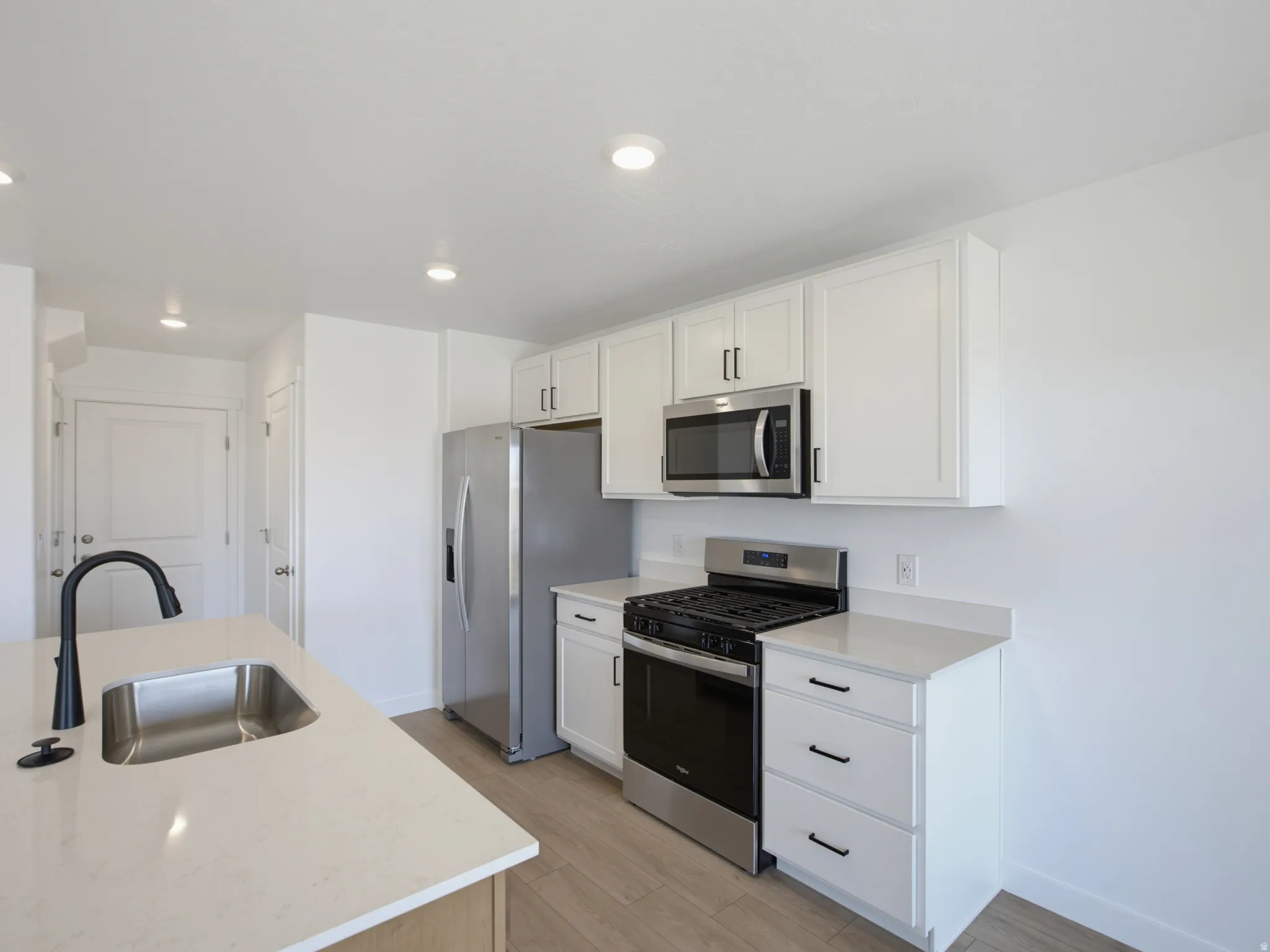 Modern kitchen featuring white cabinetry, stainless steel appliances, quartz countertops, and wood-finish flooring