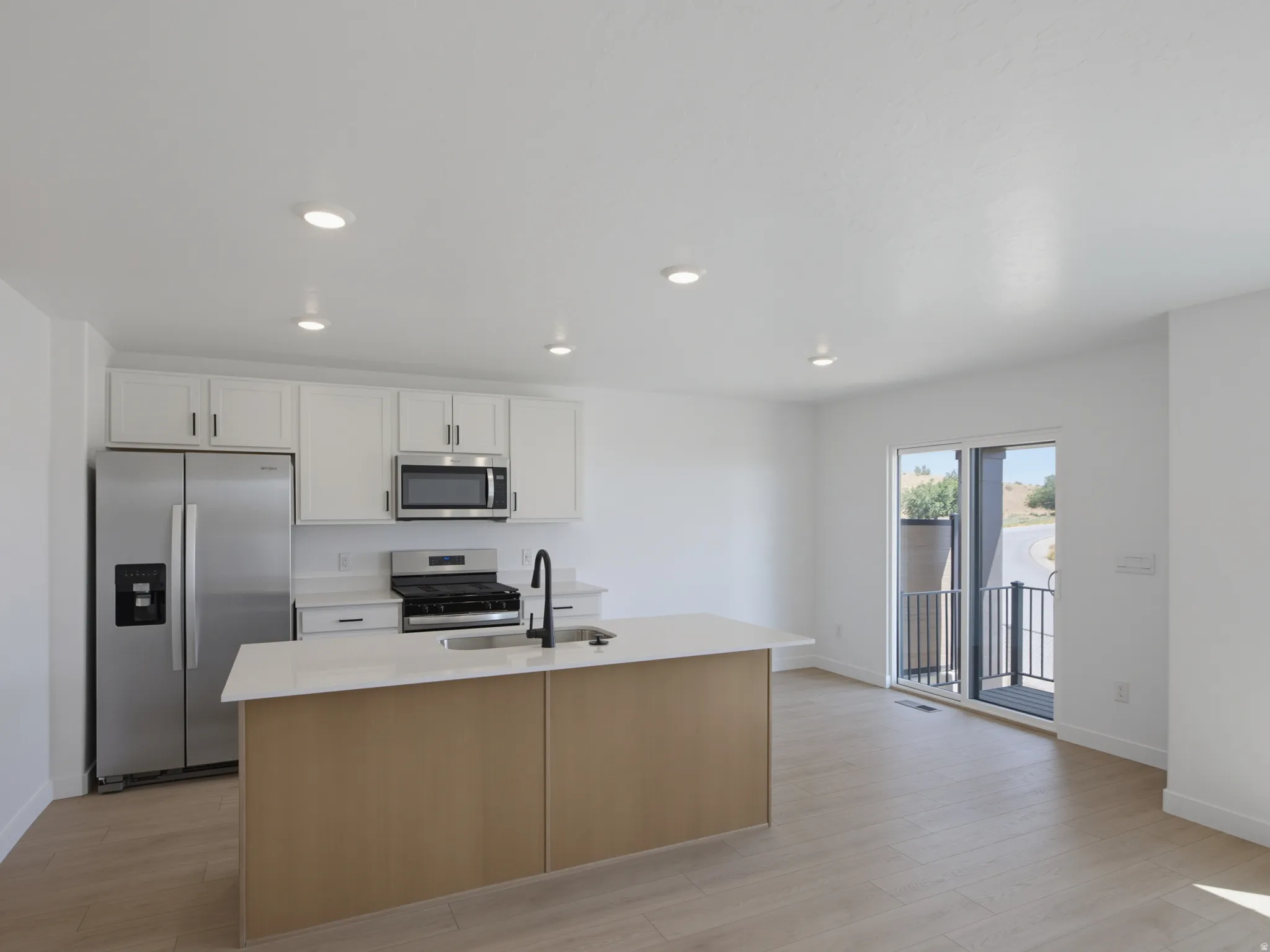 Kitchen featuring stainless steel appliances, white cabinetry, a central island with an integrated sink, and wood-finish flooring
