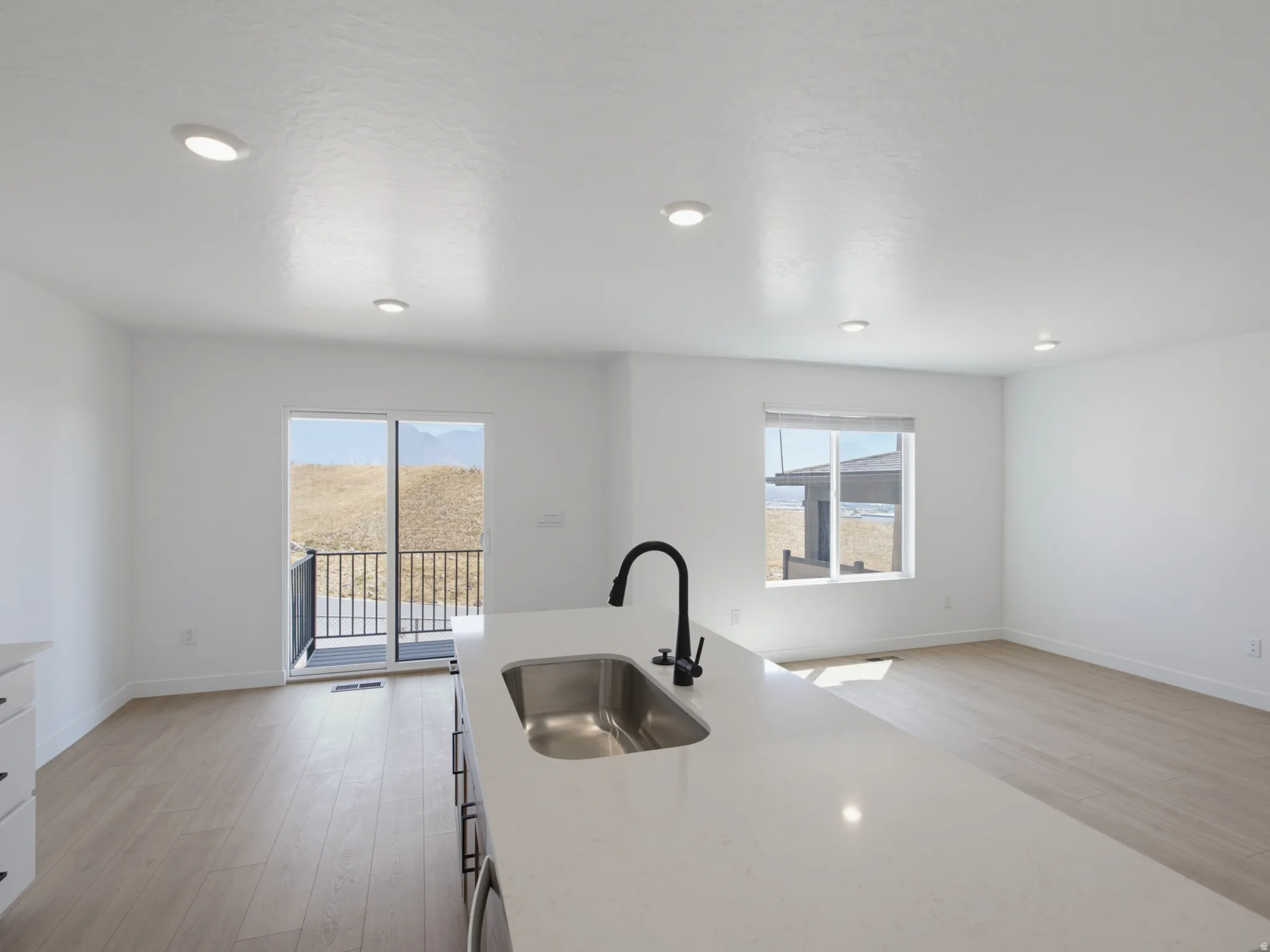 Kitchen island with an undermount sink and matte black faucet, recessed lighting, wood-finish flooring, and a sliding glass door to a balcony