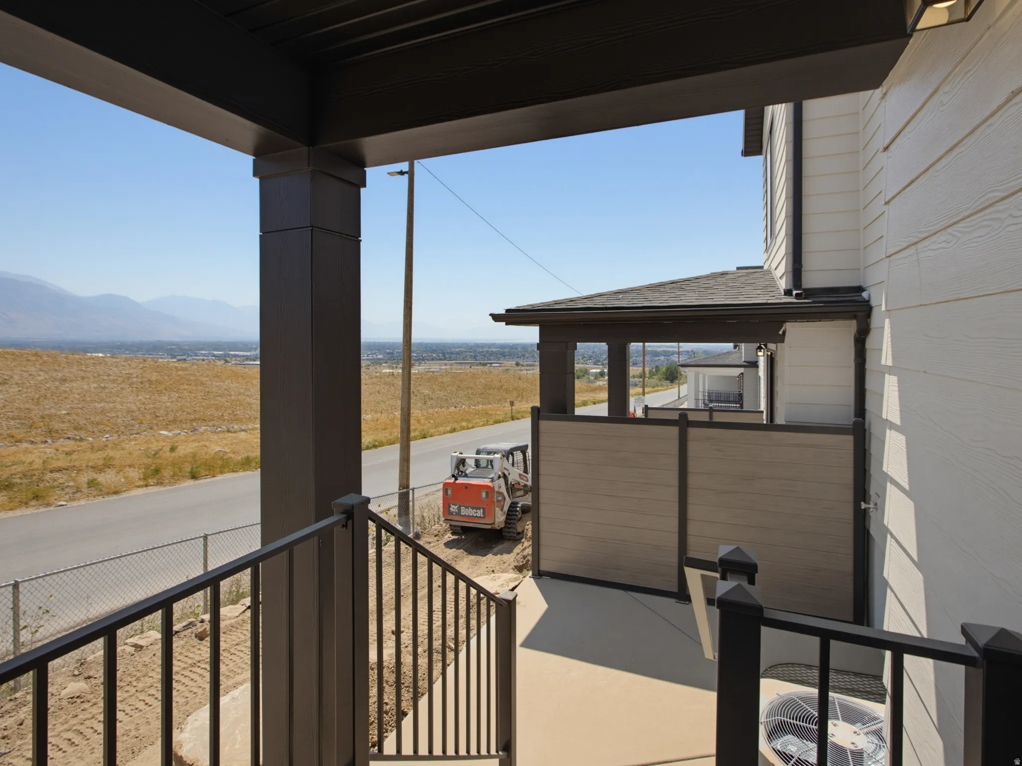 Exterior siding, dark trim, black metal railing, concrete patio, and privacy screening