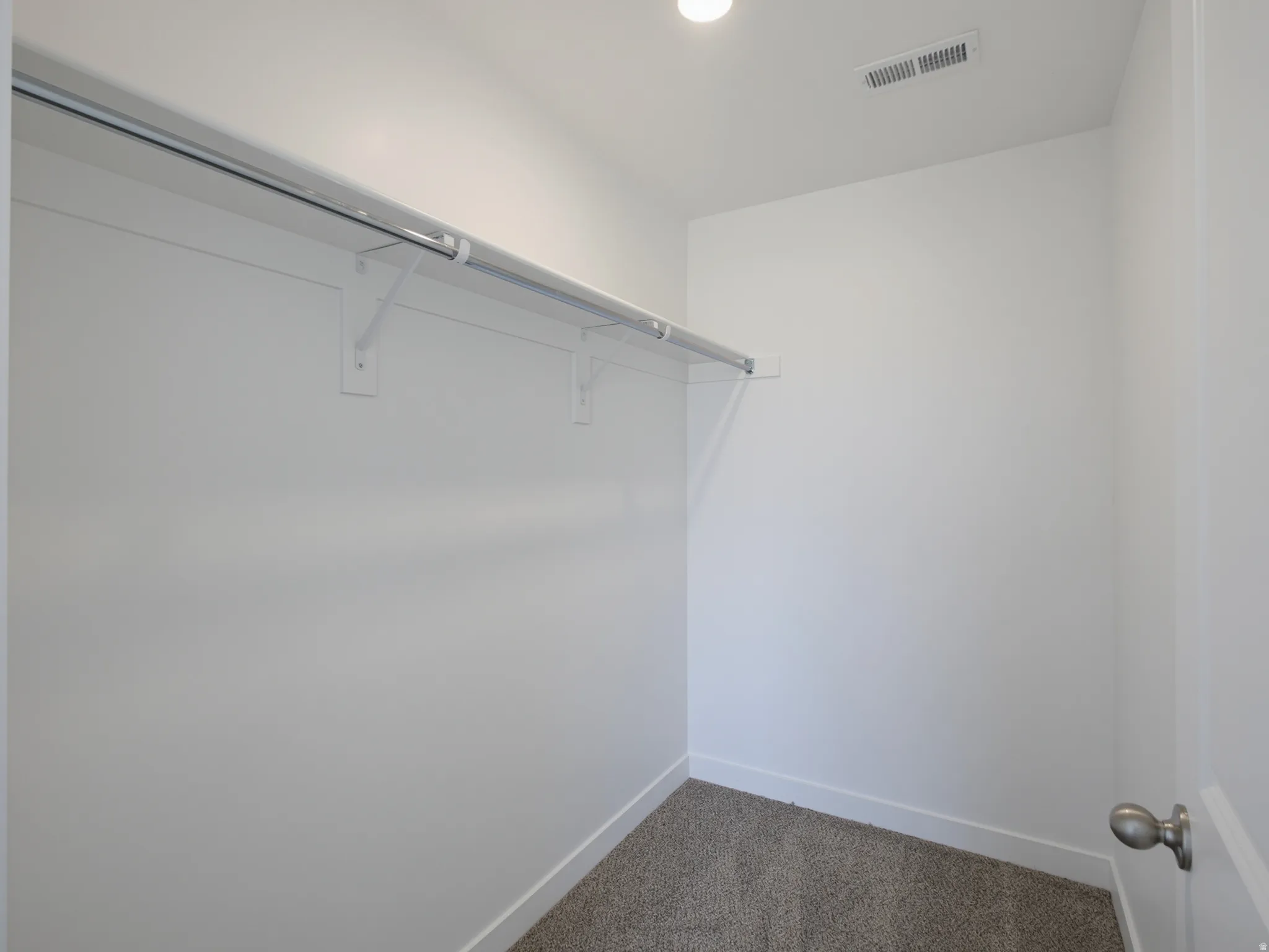 Recessed ceiling light with textured carpet flooring, painted walls, and a built-in closet rod with shelving