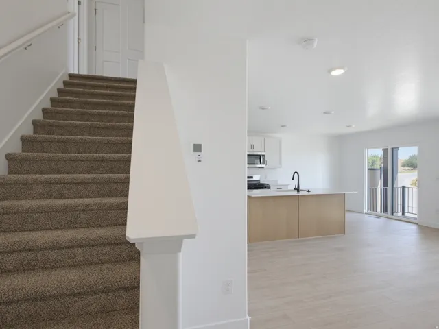Carpeted staircase with white handrail, recessed lighting, wood-finish flooring, white cabinetry, and a kitchen island with a black faucet