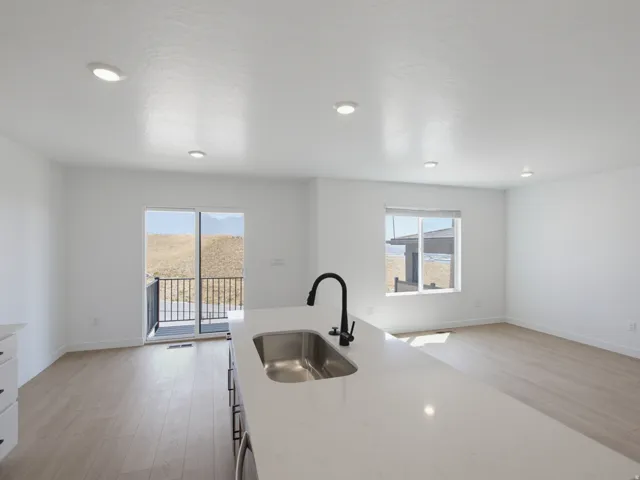 Kitchen island with an undermount sink and matte black faucet, recessed lighting, wood-finish flooring, and a sliding glass door to a balcony