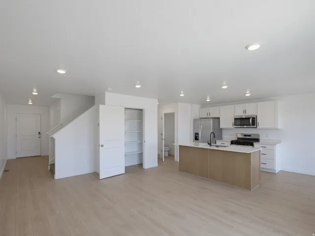 Open-concept living area with wood-finish flooring, recessed lighting, and a kitchen featuring white cabinetry, stainless steel appliances, and a central island with a sink