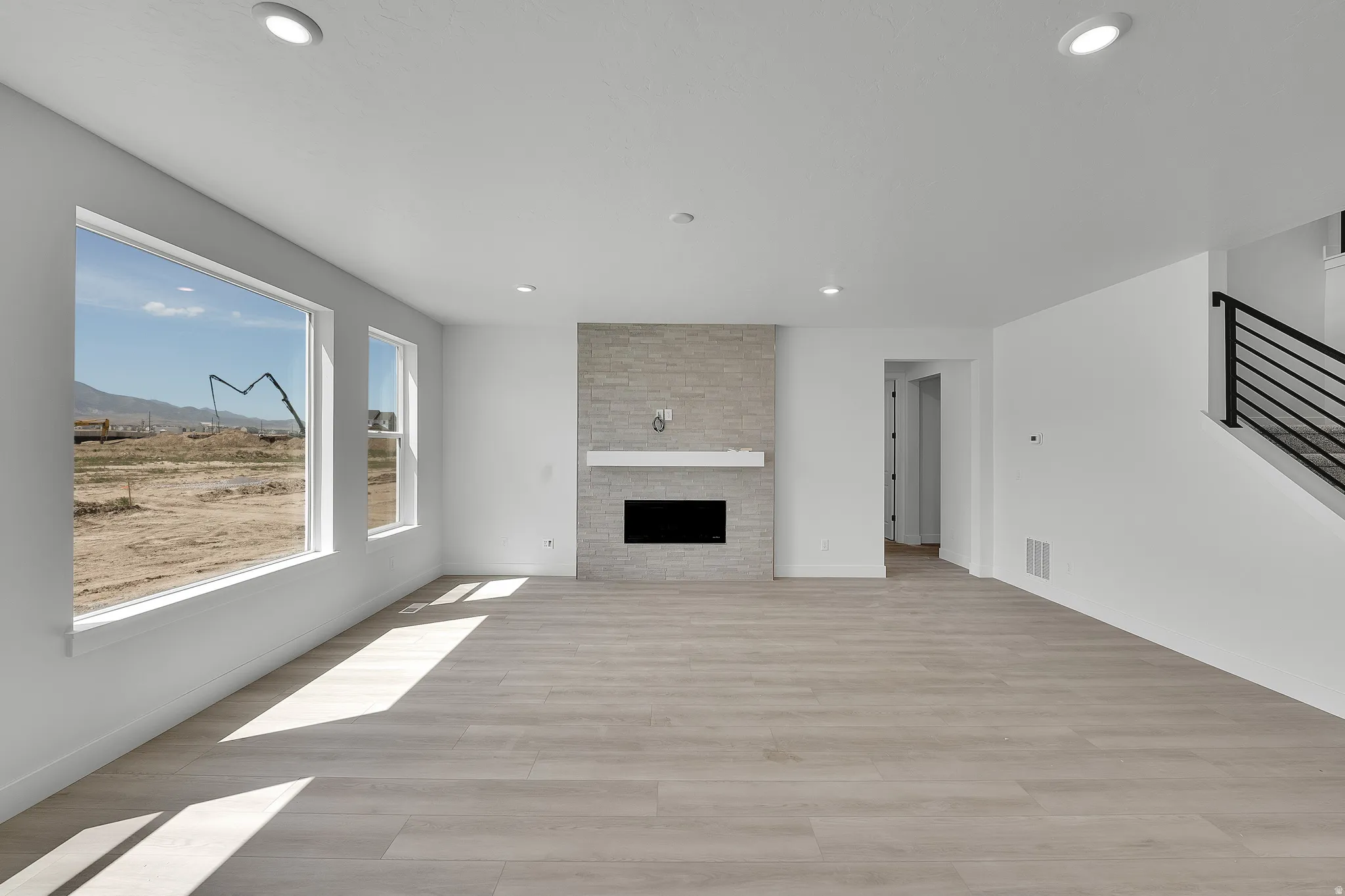 Recessed lighting, wood-finish flooring, stone-clad fireplace with mantel, built-in electric fireplace, and modern black horizontal stair railing