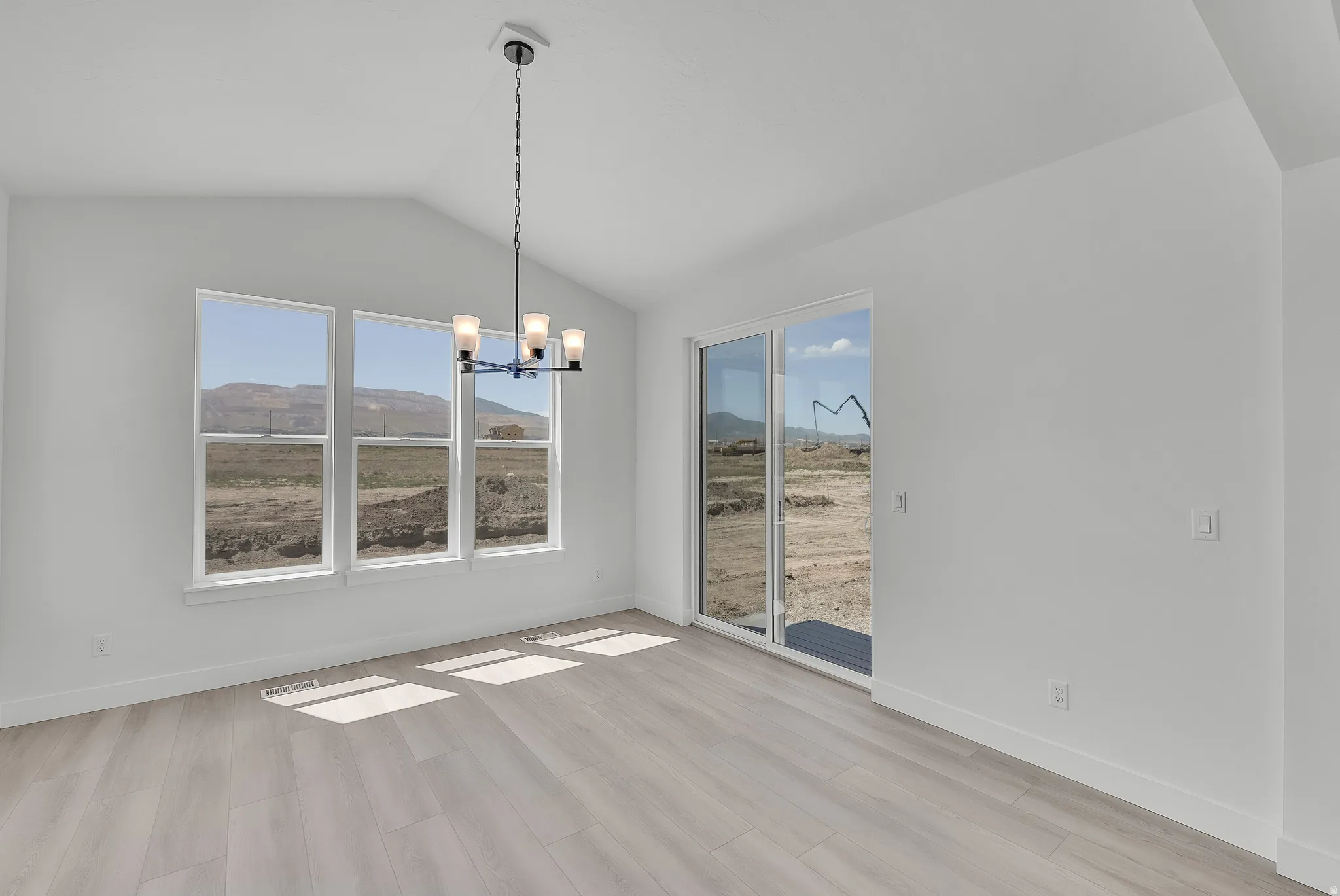 Vaulted ceiling with a contemporary chandelier, multiple large windows, light wood-finish flooring, and a glass sliding door