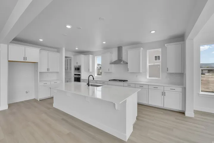 Kitchen featuring white shaker cabinetry, an expansive center island, a stainless steel range hood, light-toned wood-finish flooring, and recessed lighting