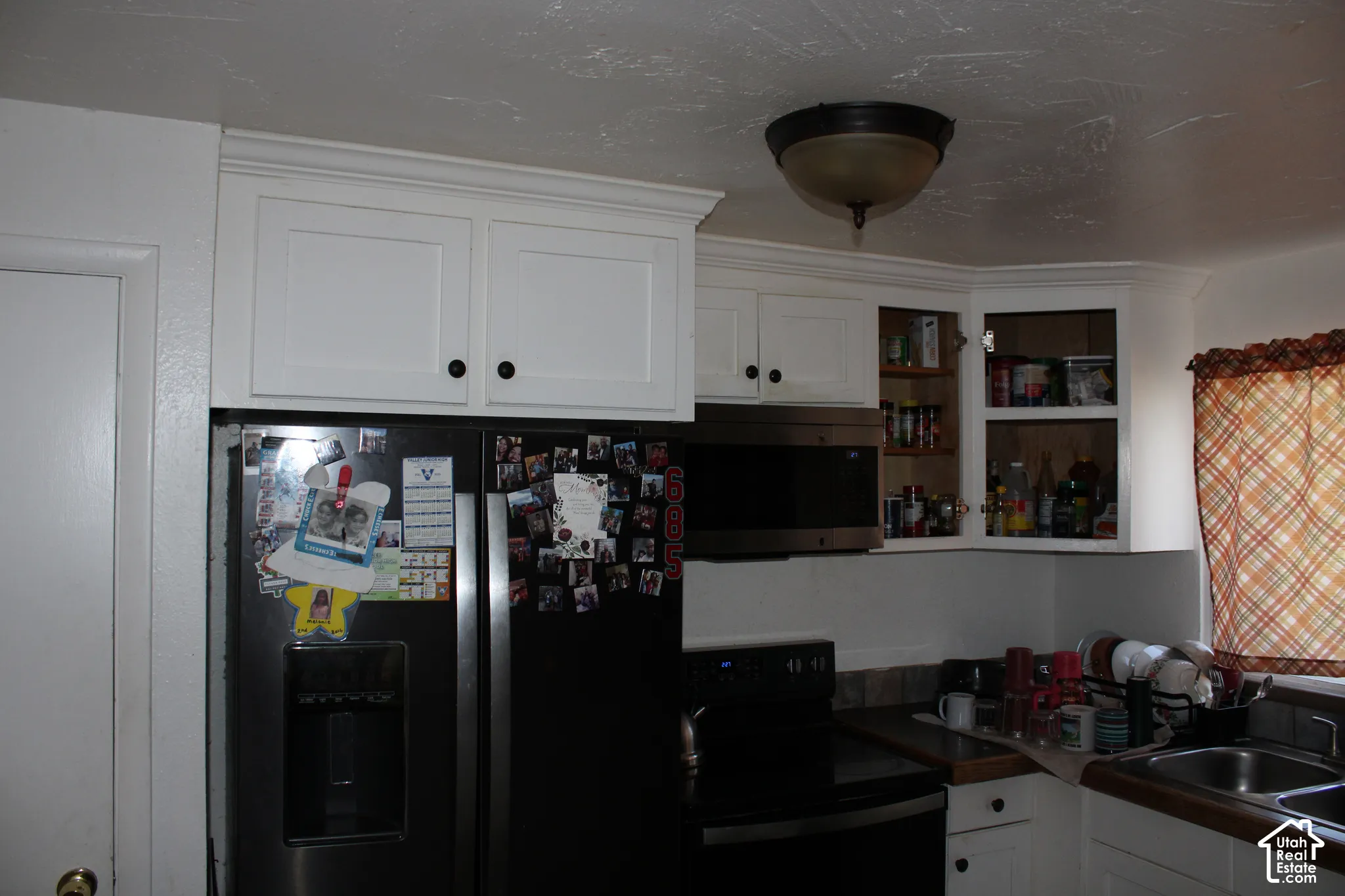 White cabinetry, stainless steel microwave, and built-in sink with dark-toned countertop