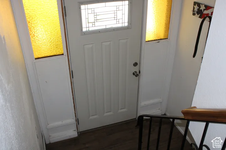 White paneled entry door with decorative glass, flanked by sidelights with textured amber glass, and wood-finish flooring