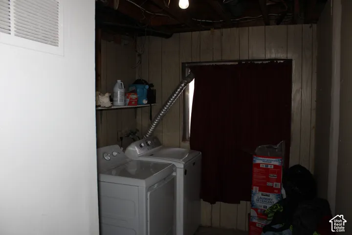Laundry area featuring wood paneling, exposed ceiling joists, and a bare bulb light fixture