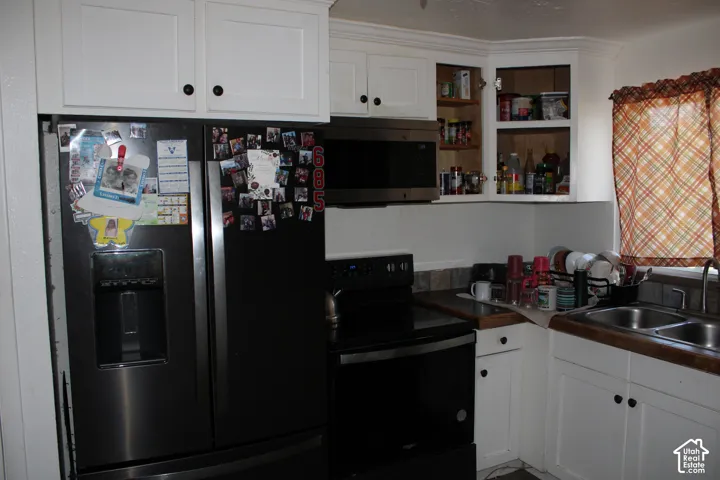 White cabinetry with black hardware, black appliance suite, dual basin sink, and wood-finish countertops