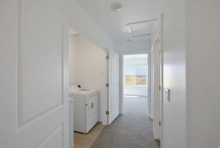 Hallway featuring light gray carpeting, white painted walls, and a laundry area with wood-finish flooring