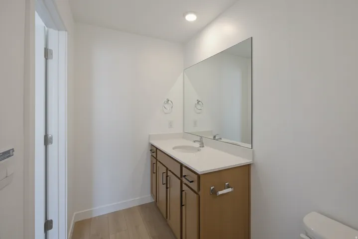 Vanity with a light wood-finish, undermount sink, solid surface countertop, and large wall-mounted mirror