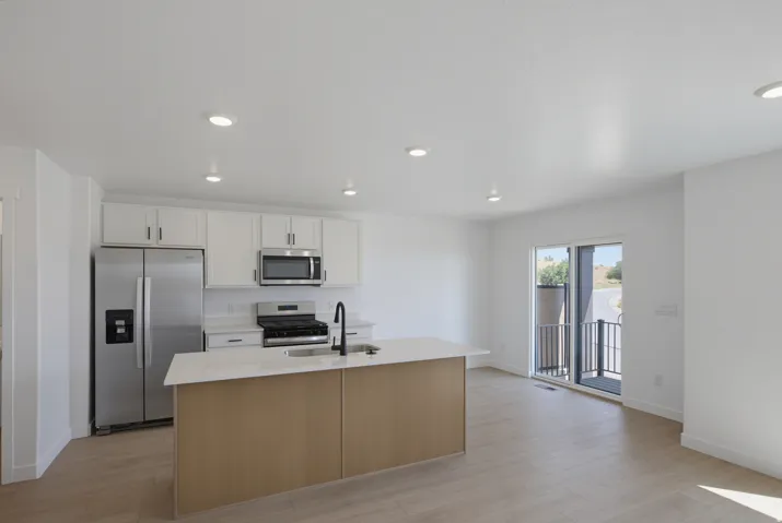 Kitchen featuring stainless steel appliances, white cabinetry, a central island with a light-toned countertop, and wood-finish flooring