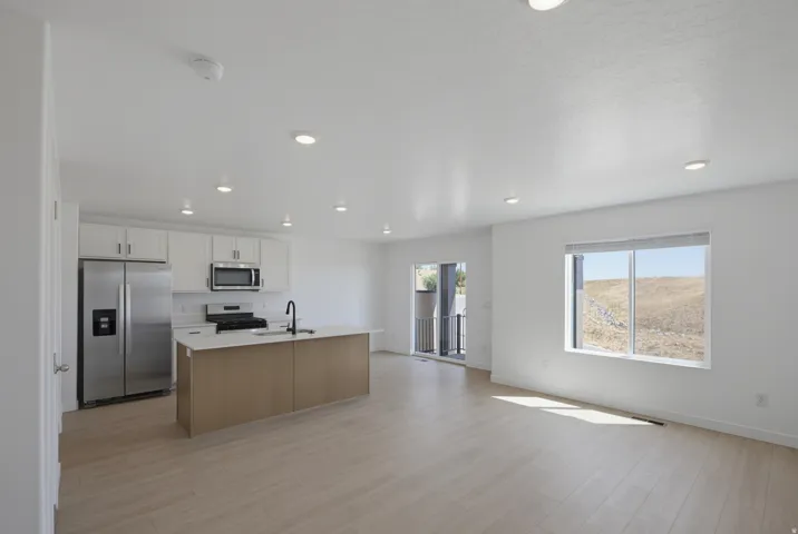 Open-concept living space with wood-finish flooring, recessed lighting, and a kitchen island featuring a sink with a matte black faucet