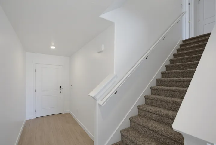 Light wood-finish flooring, recessed ceiling lighting, white interior door, carpeted staircase, and white handrail