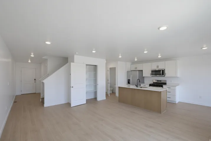 Open-concept living space featuring wood-finish flooring, recessed lighting, and a kitchen with an island, white cabinetry, and stainless steel appliances