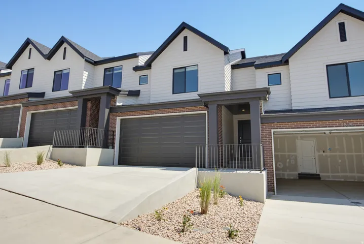 Contemporary townhome exterior featuring white siding, dark trim, gabled rooflines, brick accents, and attached garages