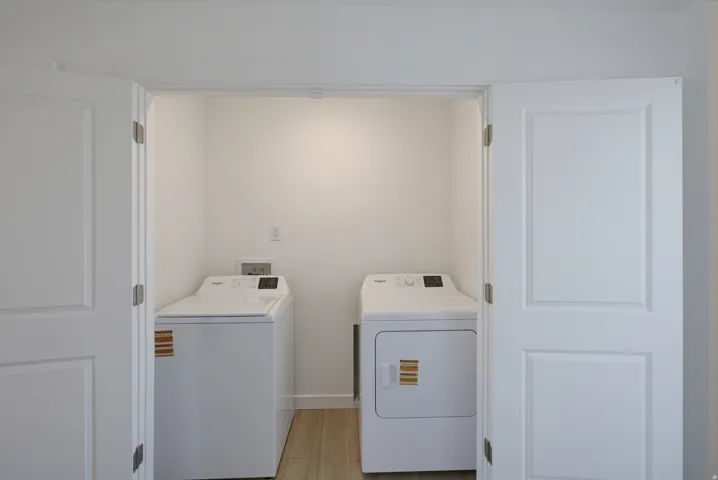 Laundry area featuring a top-load washing machine, a front-load dryer, and wood-finish flooring