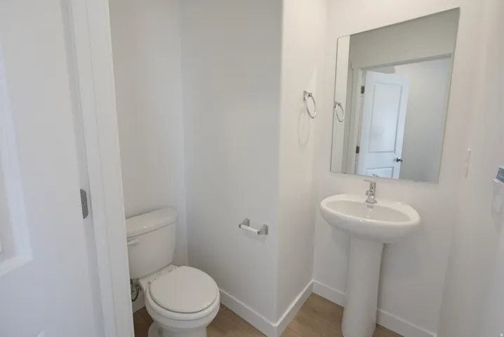 Pedestal sink with chrome faucet, wall-mounted mirror, white toilet, and wood-finish flooring