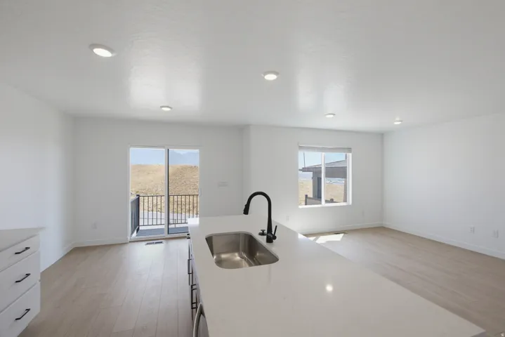 Open-concept living area featuring a kitchen island with a stainless steel sink and matte black faucet, recessed lighting, wood-finish flooring, and a sliding glass door leading to a balcony