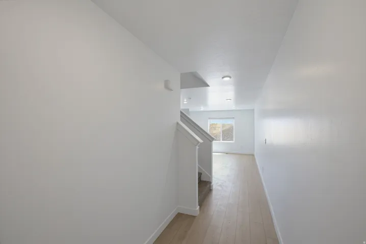 Wide hallway featuring wood-finish flooring, recessed lighting, and a staircase with white railing