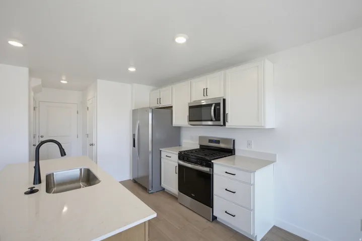 Kitchen featuring a stainless steel appliance suite, white cabinetry, light-toned countertops, and an undermount sink with a matte black faucet