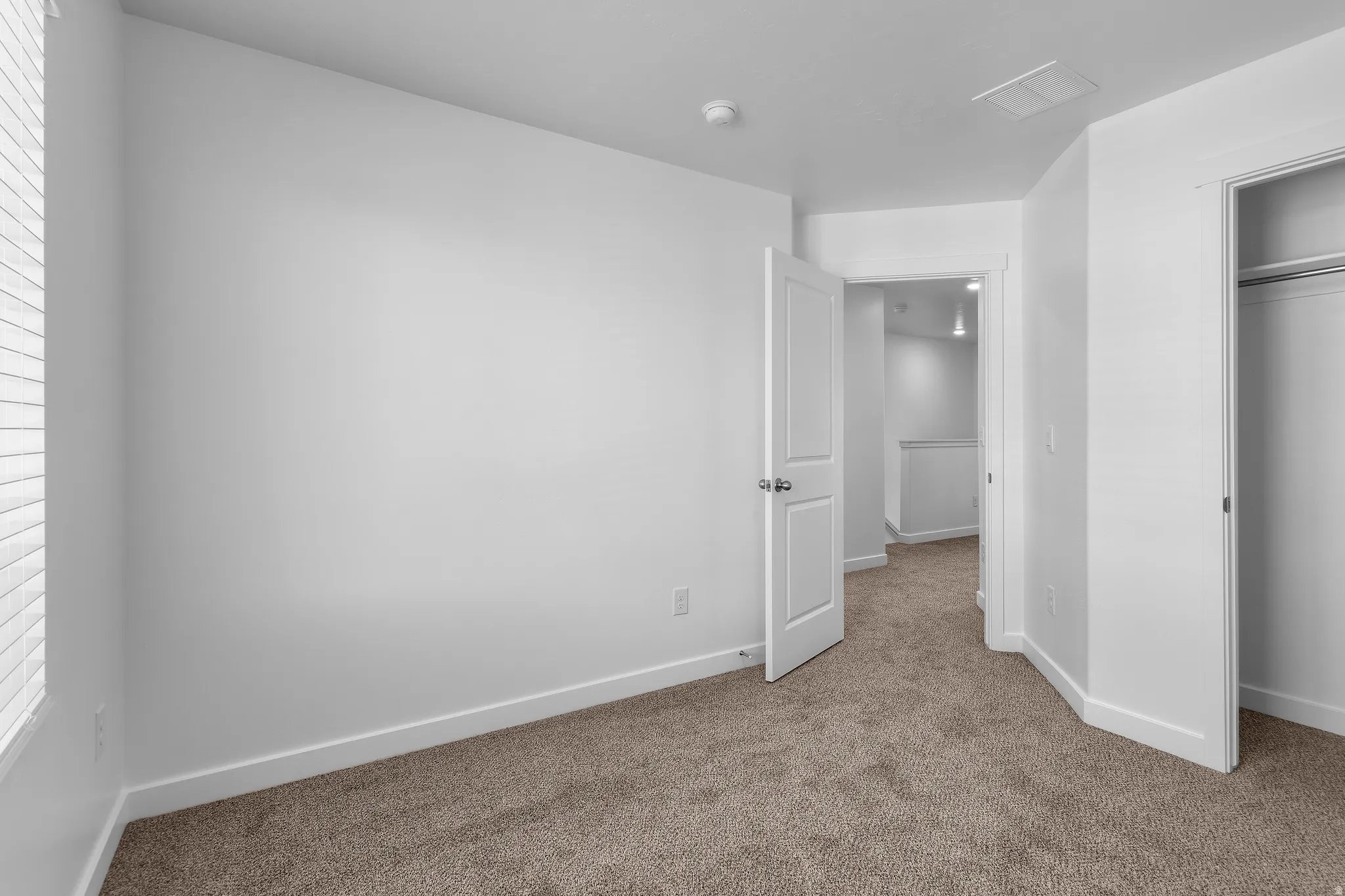 Neutral wall color, carpeted flooring, window with horizontal blinds, solid core door, and an open closet