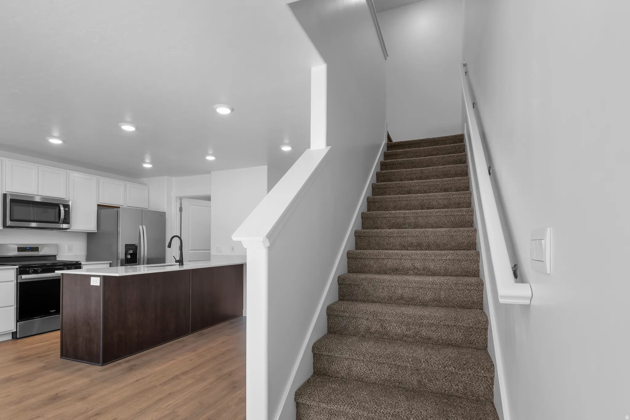 Kitchen featuring recessed lighting, stainless steel appliances, a center island with a black faucet, and wood-finish flooring