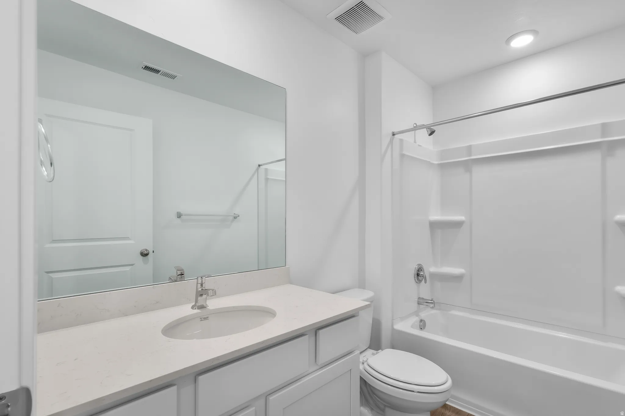 Bathroom featuring a white vanity with an undermount sink, a light-toned countertop, a large wall mirror, and a white bathtub with an integrated shower