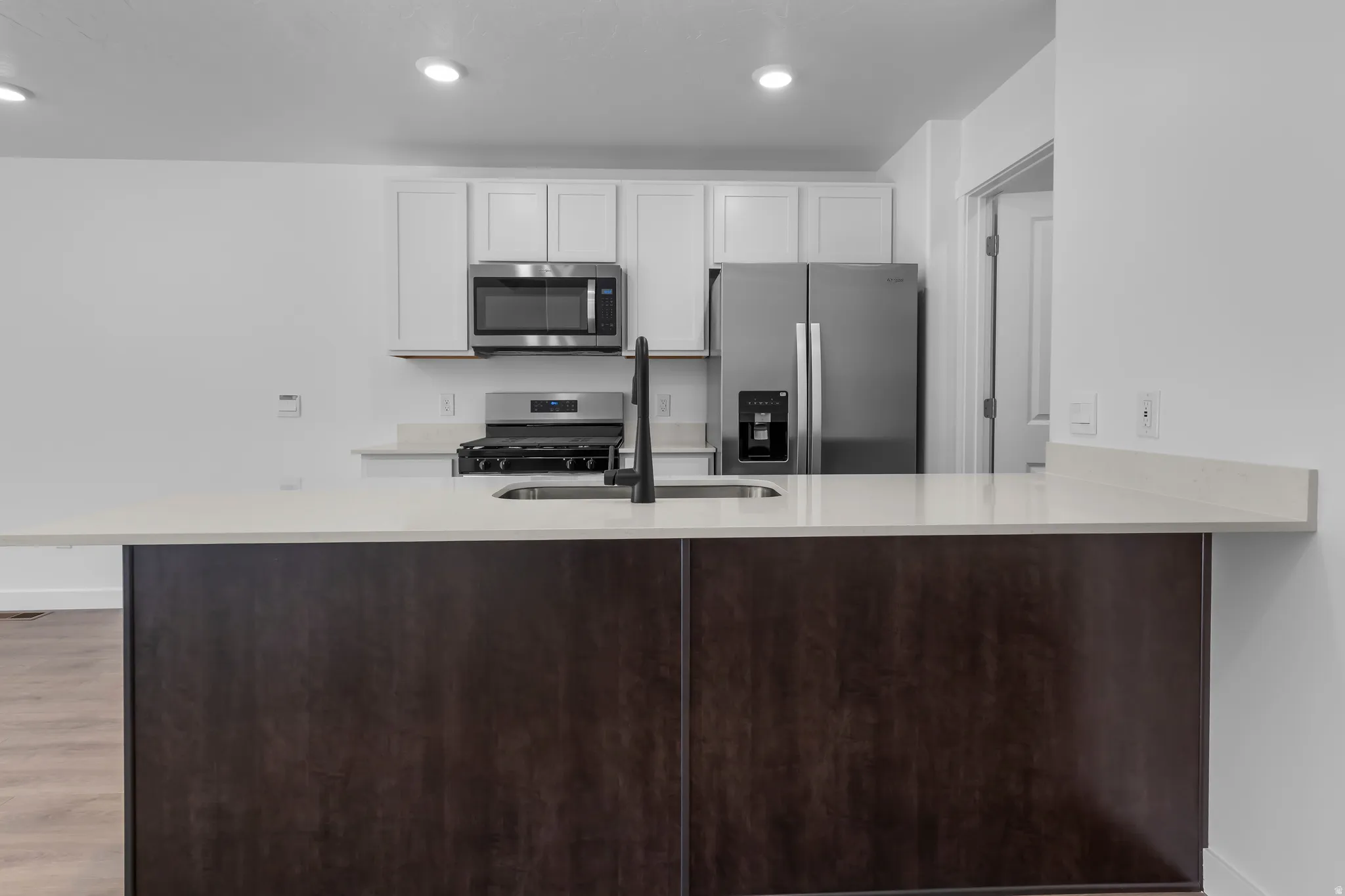 Kitchen featuring a central island with a light-toned countertop, stainless steel appliances, white upper cabinetry, and recessed lighting
