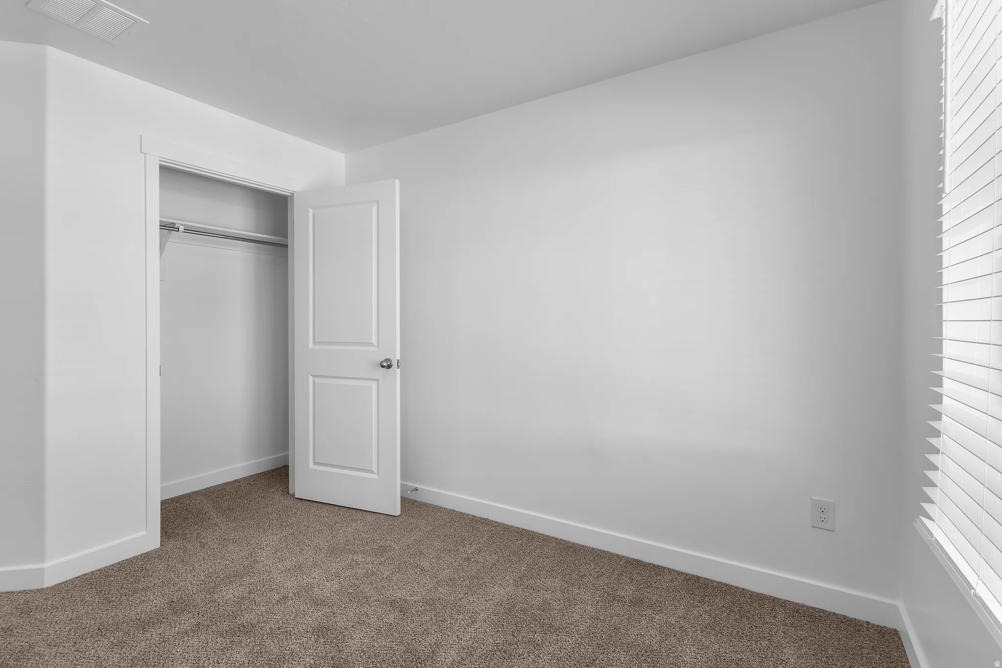 Plush carpet flooring, white walls, and a built-in closet with a hanging rod