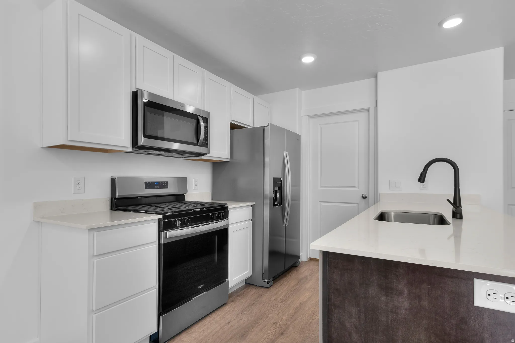 Kitchen featuring white shaker cabinetry, stainless steel appliances, light-toned countertops, a stainless steel sink, and wood-finish flooring