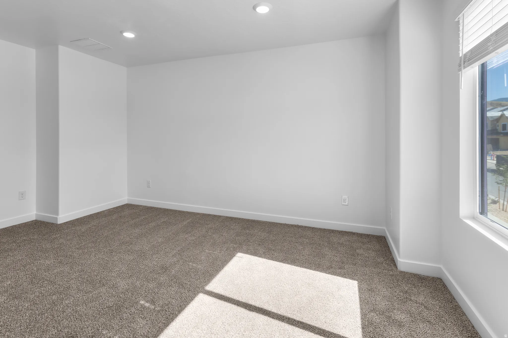 Recessed ceiling lighting, neutral tone carpet, white wall finishes, and a single window with blinds