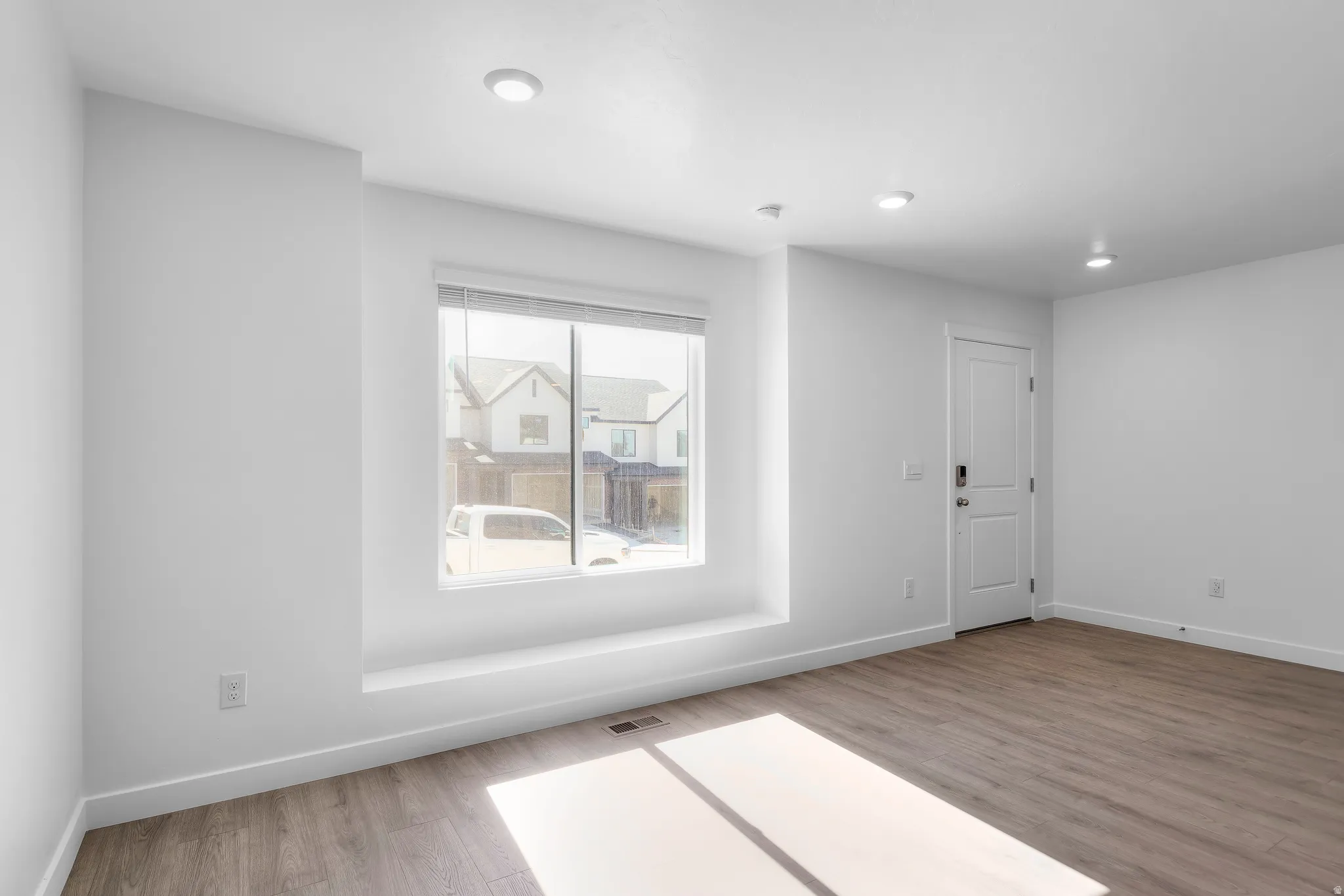 Recessed lighting illuminates this space featuring wood-finish flooring, a window with a deep sill, and a paneled door