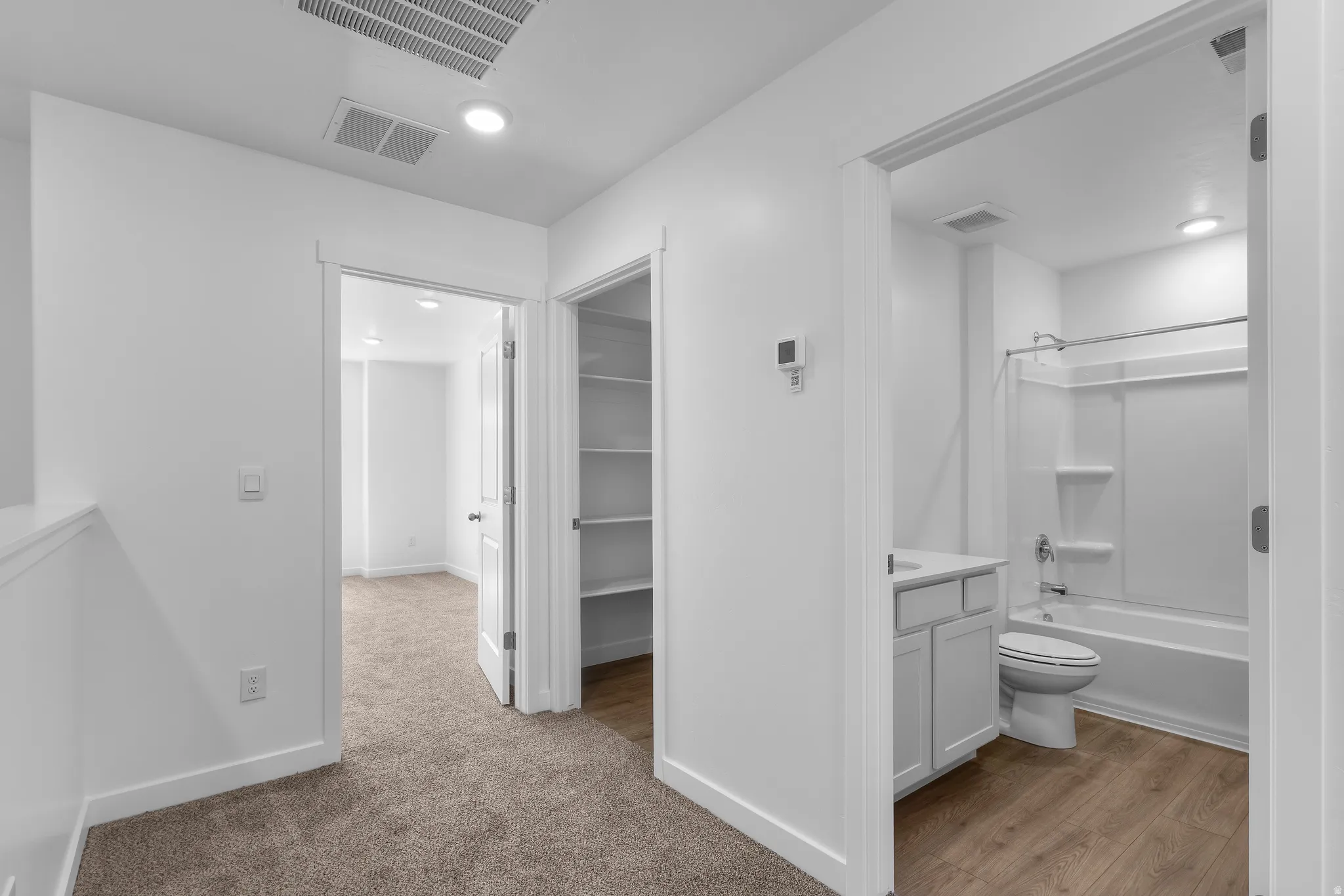 Carpeted hallway with recessed lighting, an interior room with carpeting, a built-in linen closet with shelving, and a bathroom featuring a shower-tub combination, vanity, and wood-finish flooring